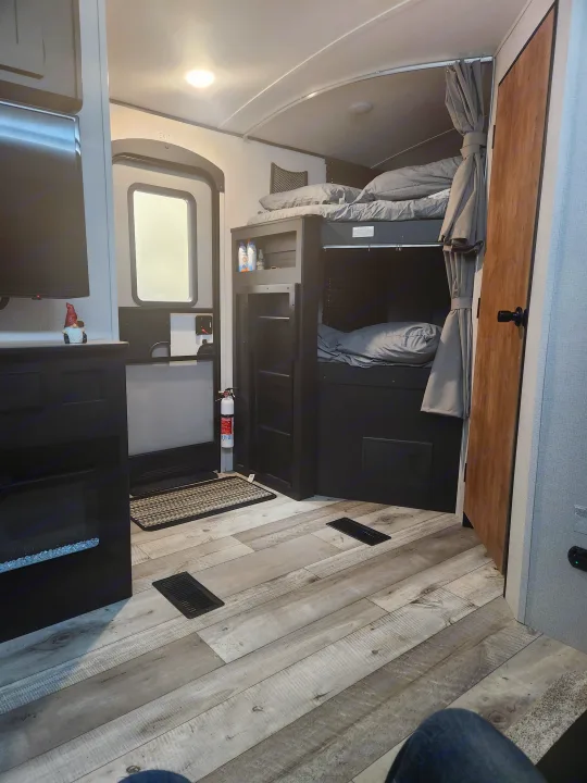 RV rental interior view: bunk beds with privacy curtains, wood-look flooring, and a safety fire extinguisher.. Keystone RV Springdale 2022