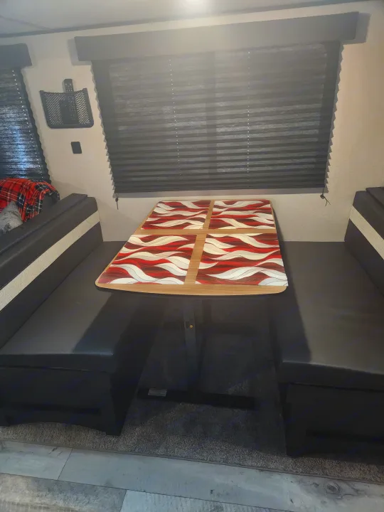 Modern RV rental dining area with a bold red and white wavy table and black benches. Dark blinds frame the window.. Keystone RV Springdale 2022