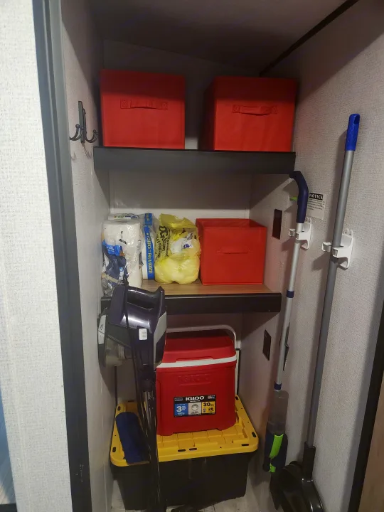 Clever RV rental storage with wall-mounted cleaning tools, an Igloo cooler, and red fabric bins for efficiency.. Keystone RV Springdale 2022