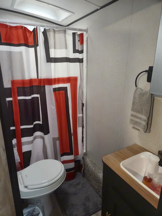 Compact RV rental bathroom featuring a colorful geometric shower curtain, white toilet, small sink, and a hand towel.. Keystone RV Springdale 2022