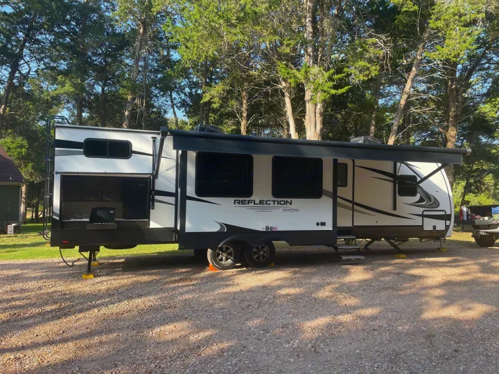This Grand Design Reflection travel trailer rv rental, with its awning extended, is parked on gravel in a shaded treeline.. Grand Design Reflection 2022