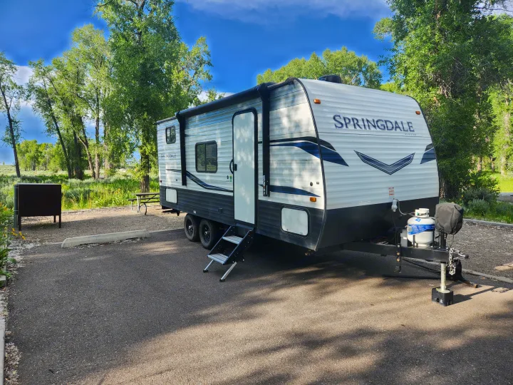 Enjoy an RV rental: a Springdale travel trailer set in a lush, green campsite under a blue sky.. Keystone RV Springdale 2022