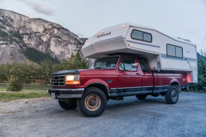 Red Ford F-250 pickup truck with a Kodiak truck camper for an RV rental adventure. Mountains in background.. Ford Other 1996