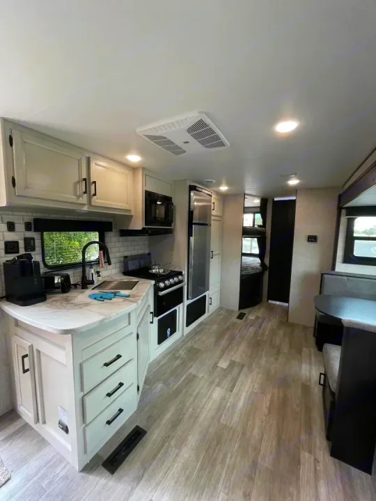 Spacious RV rental kitchen & dining area, featuring white cabinets, modern appliances, and light wood-look flooring.. Jayco Jay Flight Baja Edition 2023