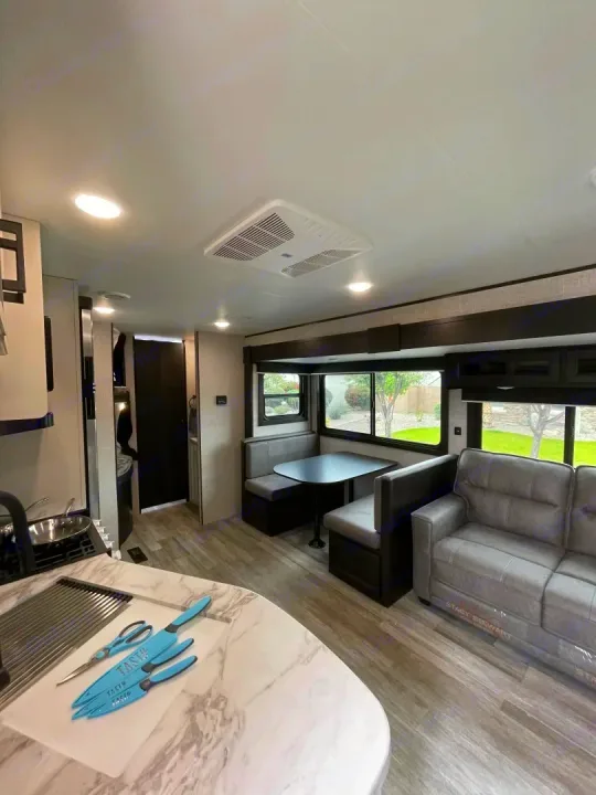 Modern RV rental interior: kitchen with light blue knives, U-shaped dinette, and grey sofa. Bright space for travel.. Jayco Jay Flight Baja Edition 2023