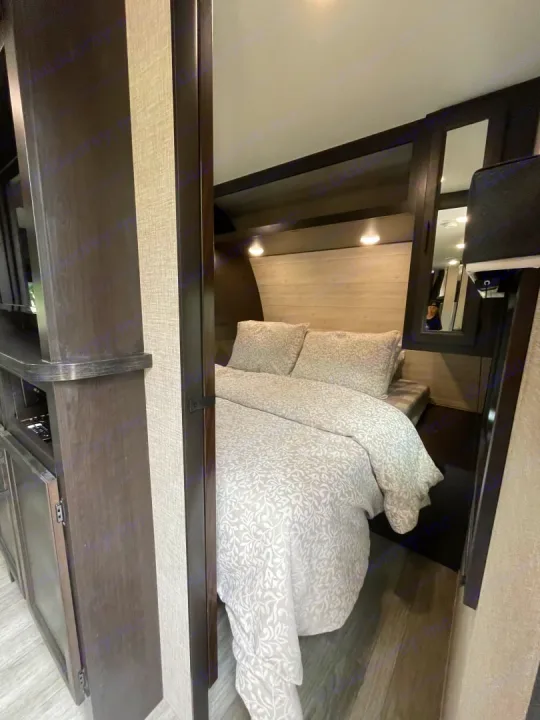 Cozy RV rental bedroom showing a bed with light bedding, wood tones, and a mirrored cabinet. Ideal for a comfortable stay.. Jayco Jay Flight Baja Edition 2023