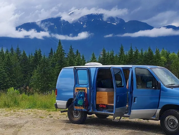 Discover adventure! This blue camper van, ready for RV rental, showcases its open interior against mountains & a forest.. Ford Econoline 2006