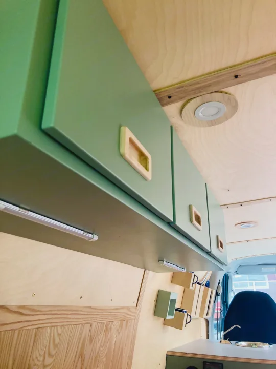 This **RV rental's** interior features sage green overhead cabinets, under-cabinet lights, and light wooden walls/ceiling.. Ford Econoline 2006