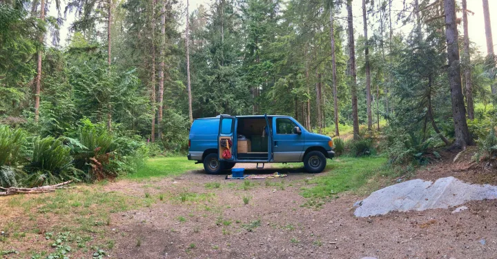 An RV rental camper van parked with its doors open in a lush forest clearing, perfect for a peaceful campout.. Ford Econoline 2006