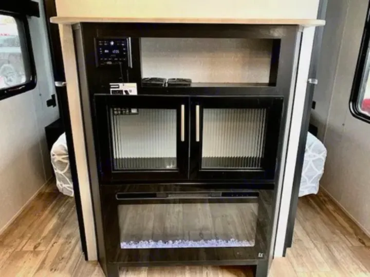 Inside an RV rental: a sleek entertainment unit with controls, glass cabinets, and a cozy electric fireplace.. Forest River Cherokee Grey Wolf 2022