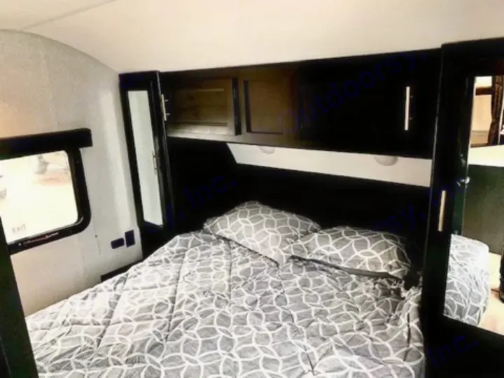 Cozy and functional bedroom inside an RV, ideal for your next rv rental. Features a bed, overhead storage, and a window.. Forest River Cherokee Grey Wolf 2022