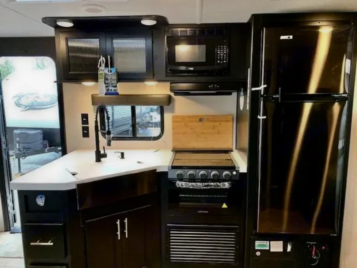 Modern RV rental kitchen with black appliances (fridge, stove, microwave), white counters, & dark cabinets.. Forest River Cherokee Grey Wolf 2022