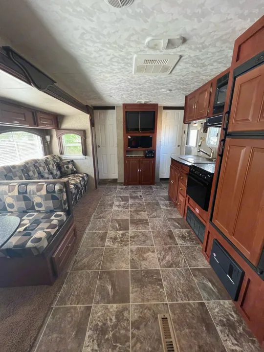 RV rental interior showing a full kitchen, patterned sofa/dinette, and entertainment center with tiled and carpeted flooring.. Forest River Wildwood 2011