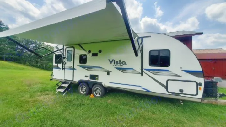 White travel trailer with extended awning on grass by a red barn. Ideal for an rv rental.. Gulf Stream Vista Cruiser 2021