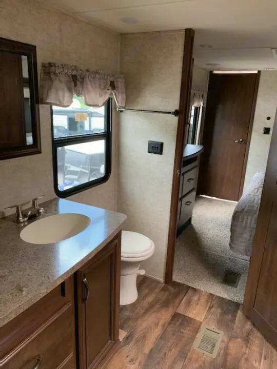 Explore this comfortable rv rental. View of a modern RV bathroom with sink, toilet, and vanity, opening to a cozy bedroom.. Forest River Sandpiper 2018