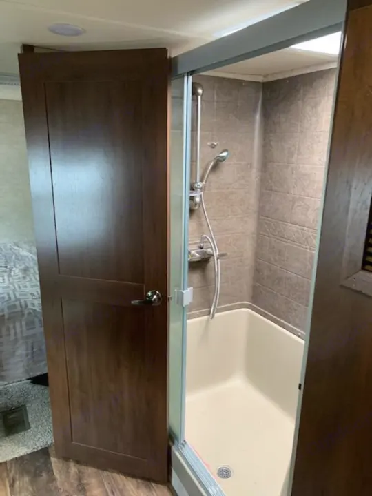 Inside this RV rental: A compact shower stall with tiled walls, glass sliding door, and showerhead, ready for your travels.. Forest River Sandpiper 2018