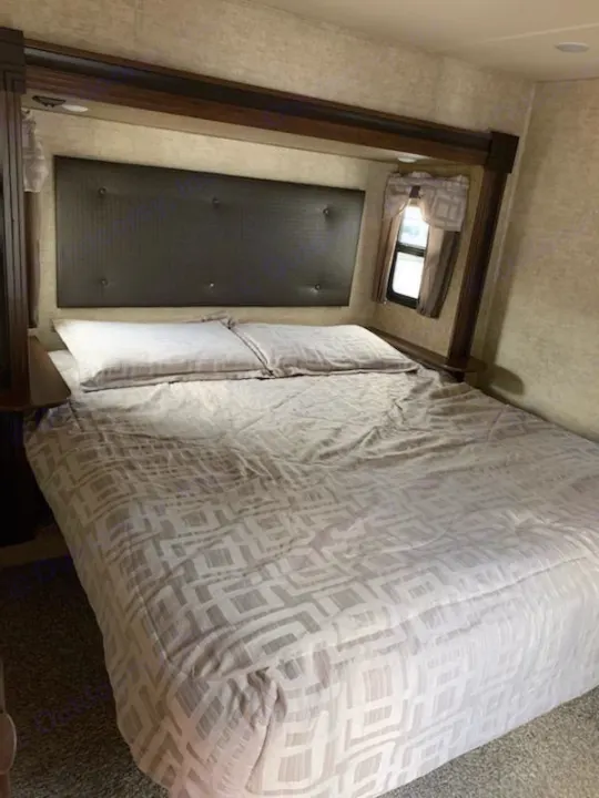 Spacious RV rental bedroom with a bed, upholstered headboard, and window.. Forest River Sandpiper 2018