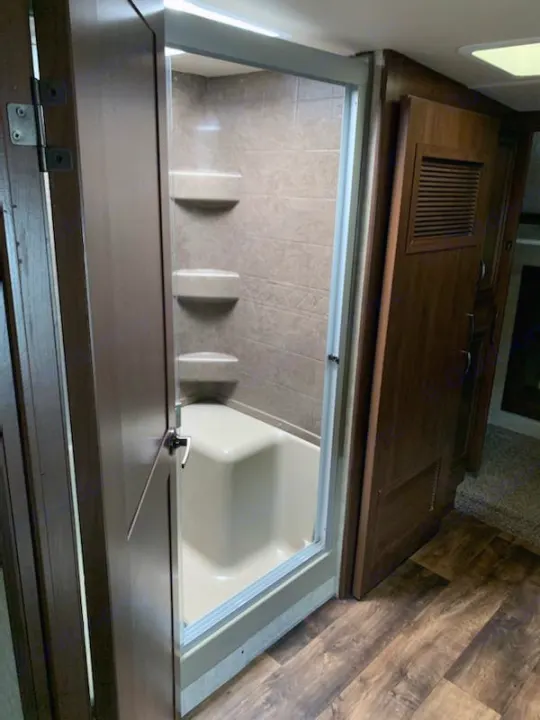 RV rental bathroom: Step-in shower with shelves, glass door, and wood-look floor.. Forest River Sandpiper 2018
