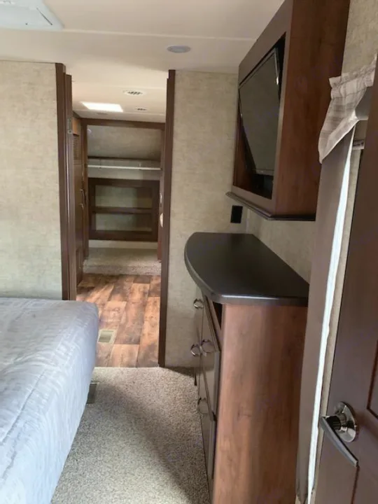 RV rental bedroom with a comfy bed, dresser, TV, and a view into the bunk room/storage area.. Forest River Sandpiper 2018
