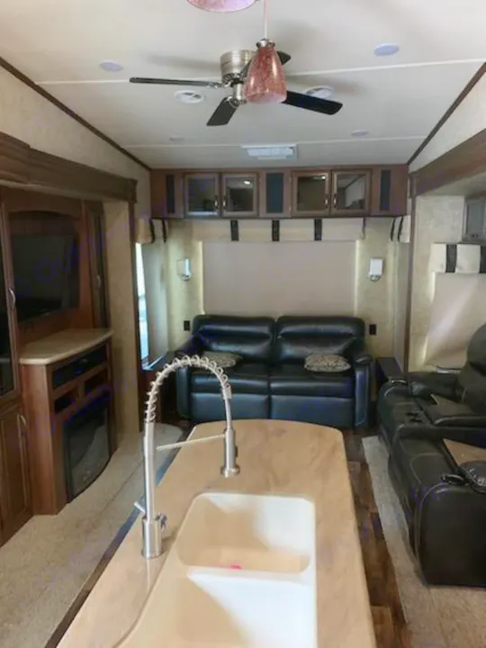 Modern RV rental interior: kitchen island, living room with black leather seating, TV, and fireplace.. Forest River Sandpiper 2018