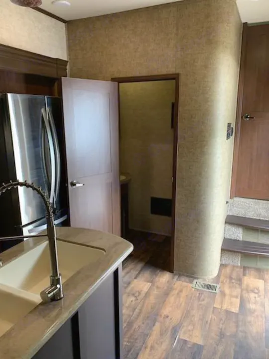 RV rental interior: Kitchen island with sink, stainless fridge, and open door to the private bath. Wood-look floors.. Forest River Sandpiper 2018