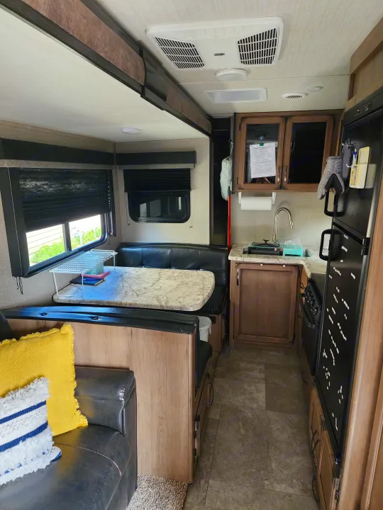 Spacious RV rental interior featuring a well-equipped kitchen, dining area, comfortable sofa, TV, and AC unit.. Grand Design Transcend 2019