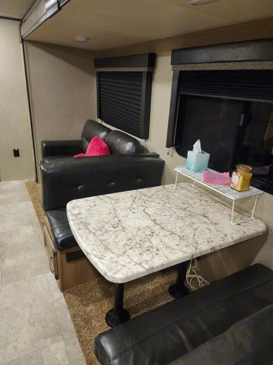 RV rental interior showing a black leather sofa, a marbled dinette table with a candle and tissue box.. Grand Design Transcend 2019