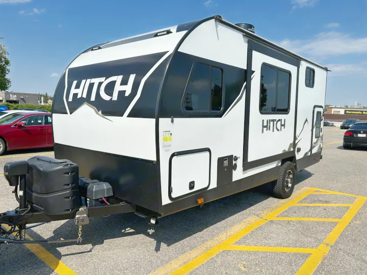 A black and white 'HITCH' travel trailer, an RV rental, prominently displayed in a sunny parking lot.. Cruiser RV Hitch 2022