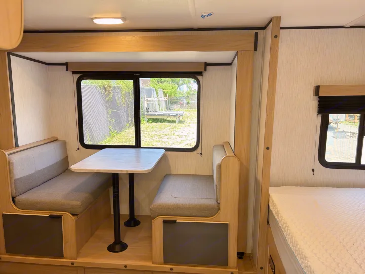 Modern RV rental interior showing a dinette with benches and table, adjacent to a comfortable bed.. Cruiser RV Hitch 2022