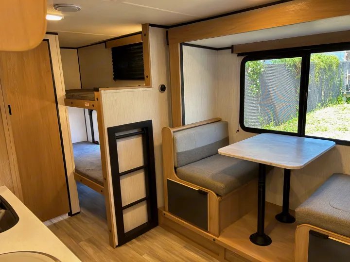 This RV rental interior shows light wood bunk beds, a grey cushioned dinette, and a large window.. Cruiser RV Hitch 2022