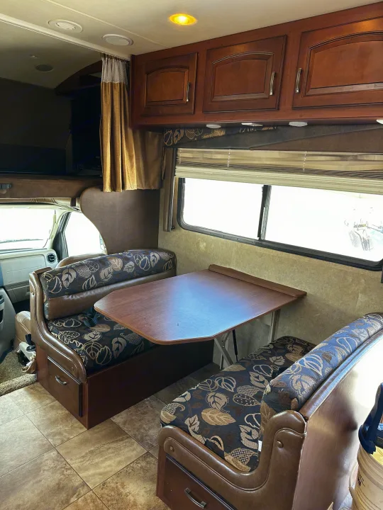 RV rental interior: A cozy dinette with patterned benches, wood table, overhead cabinets, and a bright window.. Jayco Greyhawk 2012