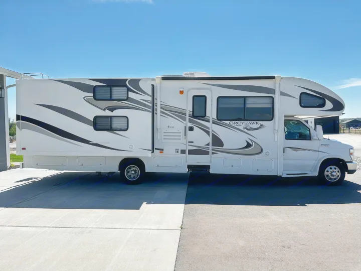 Side view of a large white Jayco Greyhawk Class C motorhome, an ideal rv rental, parked on pavement under a clear blue sky.. Jayco Greyhawk 2012