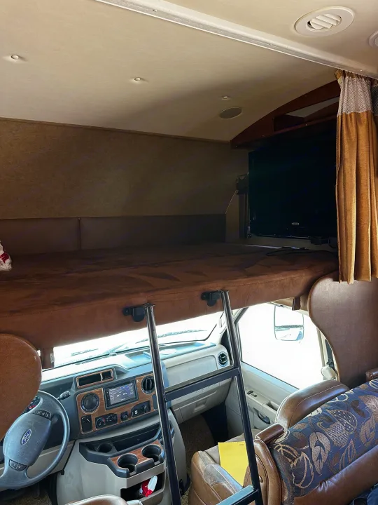 Inside this RV rental: the over-cab bunk bed with ladder, TV, and the front cockpit with dashboard.. Jayco Greyhawk 2012