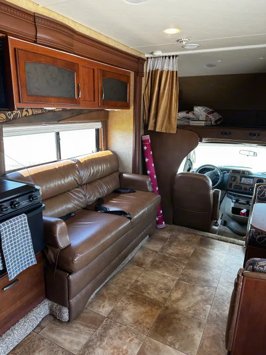 RV rental interior with a brown leather sofa, compact kitchen, and driver's cockpit leading to an overhead bunk.. Jayco Greyhawk 2012