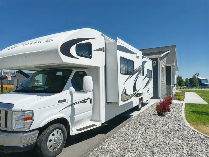 White Jayco Greyhawk RV rental parked by a modern house under a clear sky, with its slide-out extended and gravel landscaping.. Jayco Greyhawk 2012