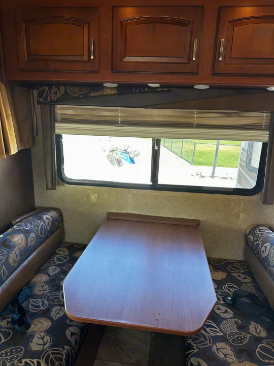 RV rental interior: dinette with a wood table, blue-patterned cushions, overhead cabinets, and large window.. Jayco Greyhawk 2012