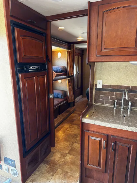 RV rental interior showcasing a compact kitchen with sink, refrigerator, and a bunk bed area for added sleeping space.. Jayco Greyhawk 2012