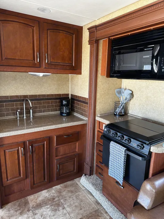 Cozy RV rental kitchen featuring warm wood cabinets, sink, microwave, stove, and tiled backsplash and floor.. Jayco Greyhawk 2012