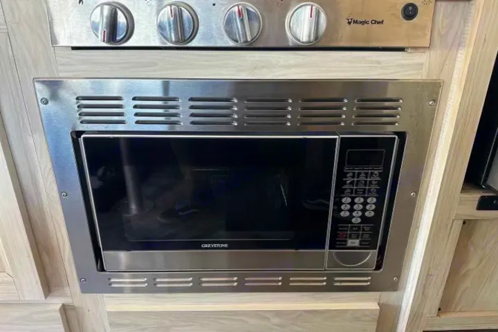 RV rental kitchen features a built-in stainless steel Greystone microwave oven below a Magic Chef range.. Forest River Sunseeker LE 2022