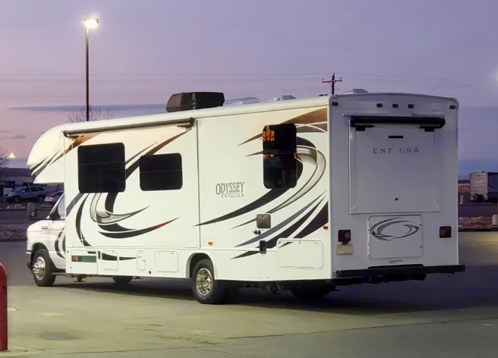 A striking white Entegra Odyssey Class C RV rental, with bold black & brown decals, is parked at twilight on asphalt.. Entegra Coach Odyssey 2021
