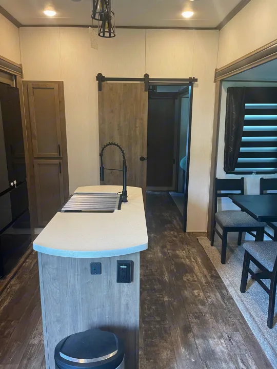 Modern RV rental interior showing a functional kitchen island, dining area, and barn door. Perfect for comfortable travels.. Forest River Sabre 2022