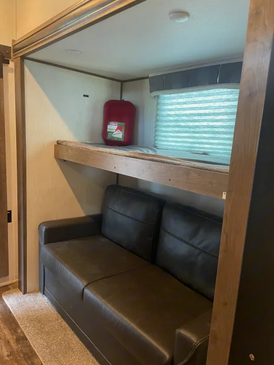 RV rental interior featuring a practical bunk bed over a dark leather sofa, with a sleeping bag on the top bunk.. Forest River Sabre 2022