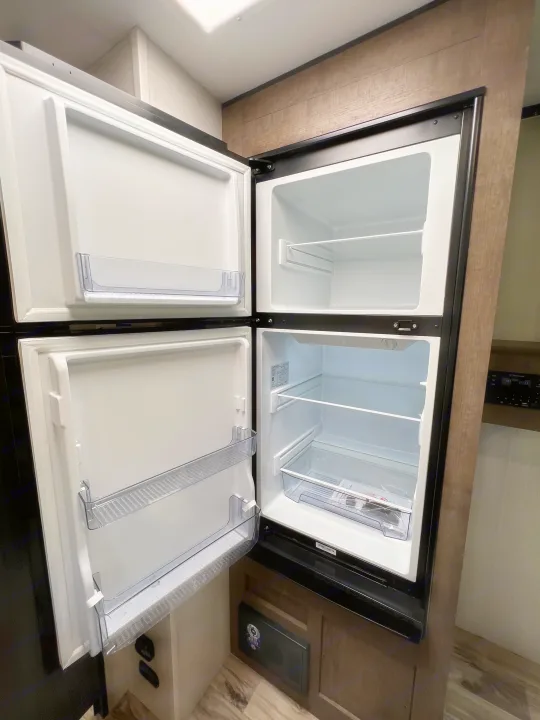 An open, clean two-door refrigerator in an RV rental, showing empty shelves and door bins, ready for your provisions.. Venture Rv Sonic 2023