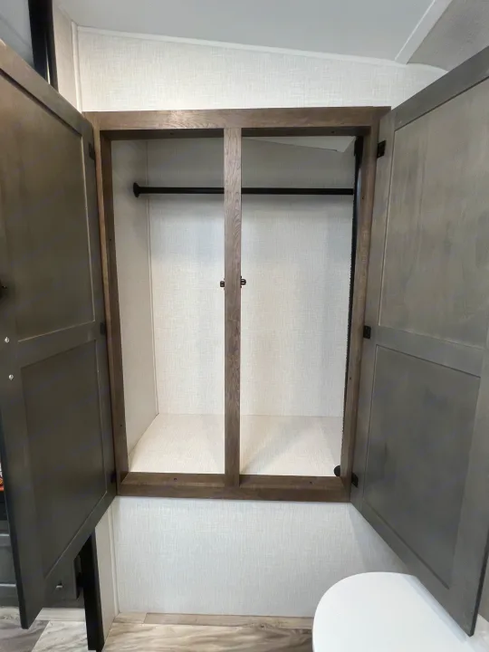 This RV rental features an open, empty wardrobe with two sections and hanging rods, offering convenient storage space for travelers.. Venture Rv Sonic 2023