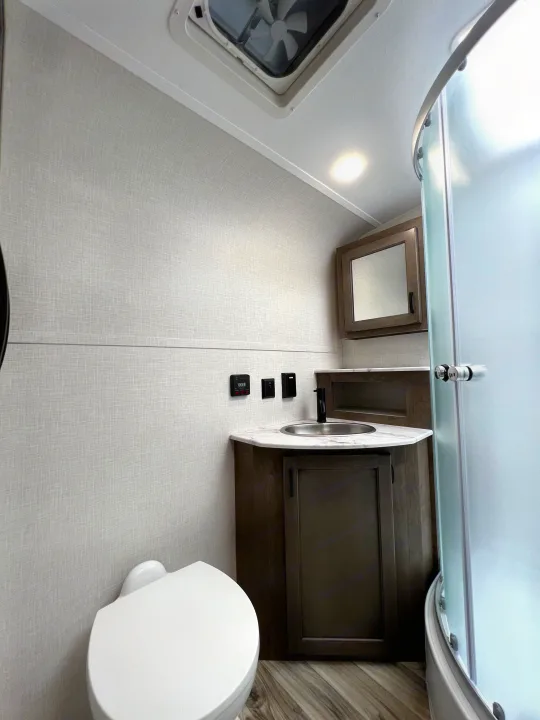 Modern RV rental bathroom interior, featuring a white toilet, vanity with sink, mirrored cabinet, and a curved glass shower stall.. Venture Rv Sonic 2023