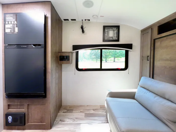Inside a clean RV rental: Furrion fridge, light sofa, window with outdoor view, and wall controls.. Venture Rv Sonic 2023