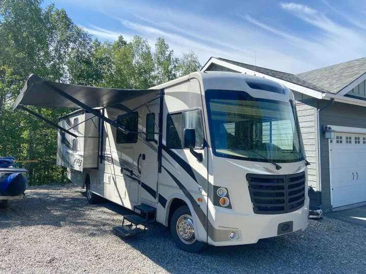 Spacious FR3 RV rental, a light-colored motorhome with extended awning, parked on a gravel drive by a house under blue sky.. Forest River Fr3 2017