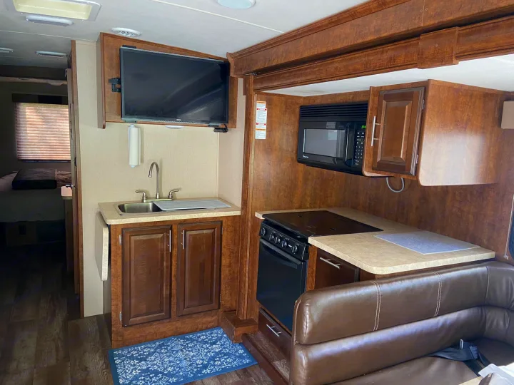 Modern RV rental kitchen & living space. Full amenities: sink, stove, microwave, TV, and brown L-shaped dinette seating.. Forest River Fr3 2017