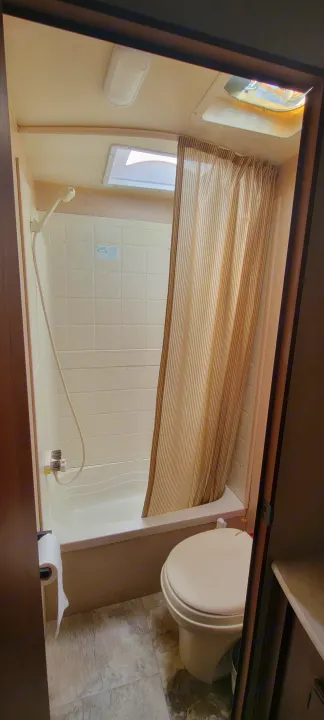 RV rental bathroom features compact shower/tub, toilet, and skylight, designed for efficient travel space.. Jayco Jay Flight SLX 2015