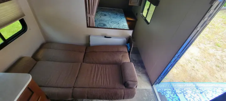 RV rental interior: Brown sofa and bedroom visible, with an open door revealing an outdoor mat and scenery.. Jayco Jay Flight SLX 2015